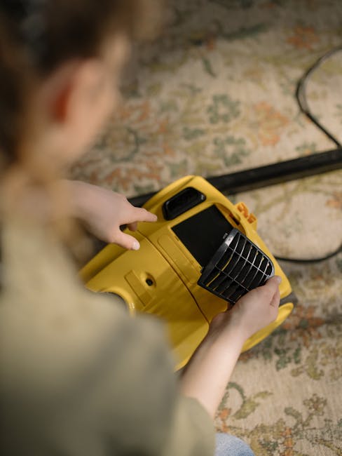 A professional cleaner from Ealing Carpet Cleaners dressed in a white protective suit, face mask, and gloves is vacuuming a plush, light beige carpet in a bright, modern living room. The room features